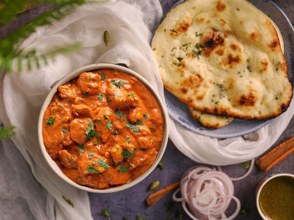 Butter Chicken in cremiger Tomatensoße, serviert mit Naan-Brot
