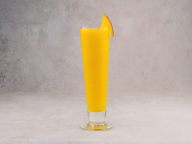 Frisch zubereitetes Mango-Lassi im hohen Glas mit einer Mangoscheibe am Rand